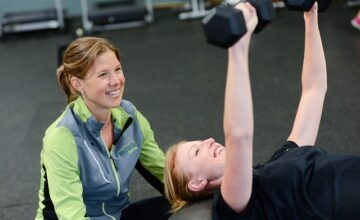 ダンベルプレスをする女性をサポートする女性トレーナー