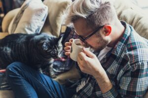 ソファの上でホットコーヒーを飲む男性とペットの猫