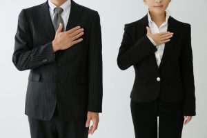 右手を胸に手を当てるスーツ姿の男女