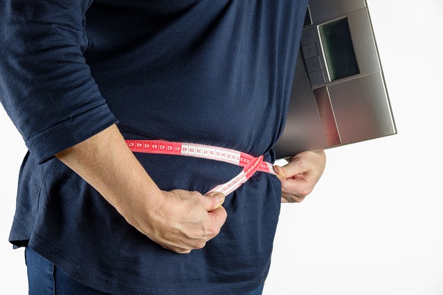 メジャーで腹囲を測定し、体重計を脇に抱える人のお腹周り