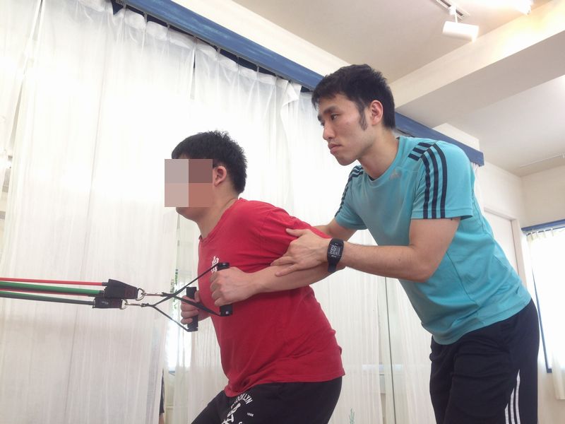 チューブを使った肘を引く運動を指導する男性
