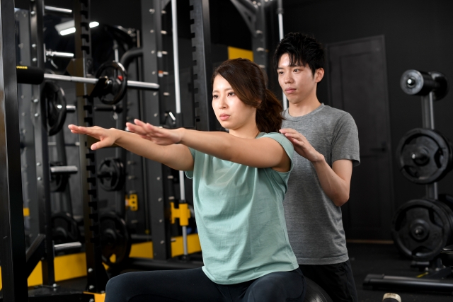 スクワットをする女性クライアントと補助する男性トレーナー