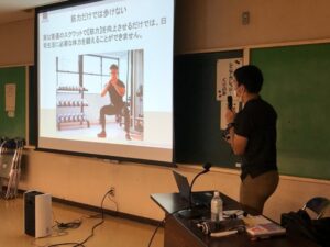 スクリーンに投影された画像を見ながら話す人